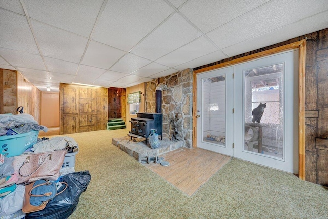 living room featuring a wood stove, a drop ceiling, and wood walls