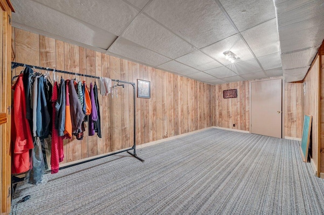 finished below grade area with a paneled ceiling, wooden walls, and carpet floors