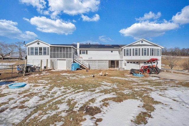 rear view of house featuring an attached garage, a sunroom, stairs, driveway, and roof mounted solar panels