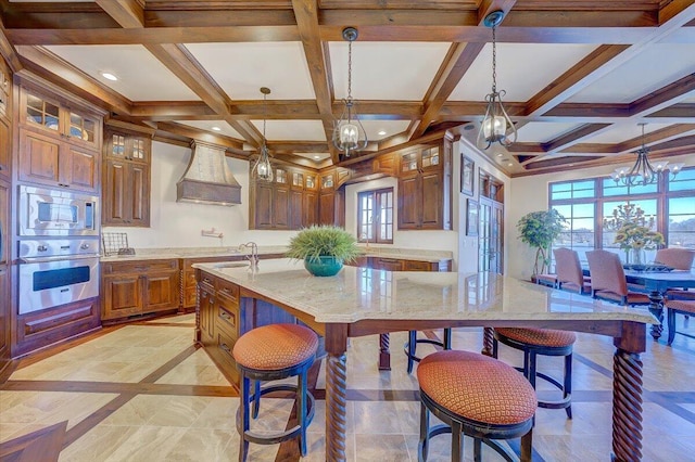 kitchen with decorative light fixtures, custom exhaust hood, light stone counters, stainless steel appliances, and a spacious island