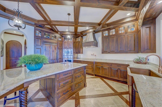 kitchen with light stone countertops, custom range hood, pendant lighting, and appliances with stainless steel finishes