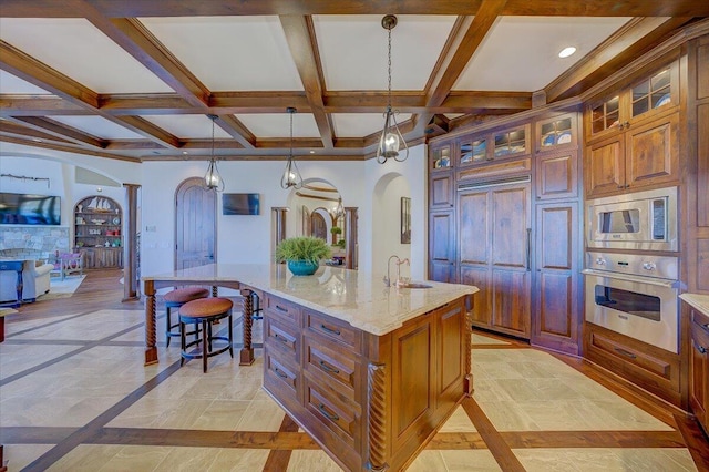 kitchen featuring pendant lighting, sink, appliances with stainless steel finishes, a kitchen island with sink, and light stone counters