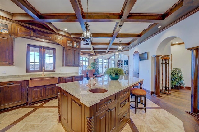 kitchen with a breakfast bar, an island with sink, sink, hanging light fixtures, and light stone countertops