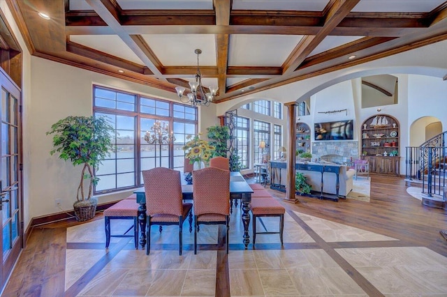 dining space featuring an inviting chandelier, built in shelves, coffered ceiling, and a high ceiling