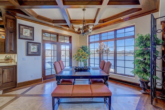 dining room with an inviting chandelier, a water view, coffered ceiling, ornamental molding, and french doors