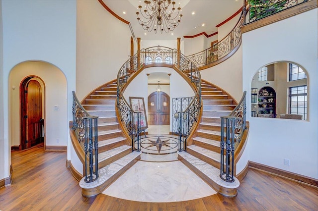 entrance foyer featuring hardwood / wood-style flooring, a towering ceiling, crown molding, and a notable chandelier