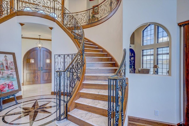 staircase featuring crown molding, a towering ceiling, and french doors