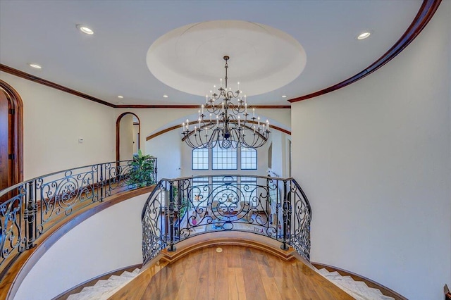 stairway with a notable chandelier, crown molding, and wood-type flooring