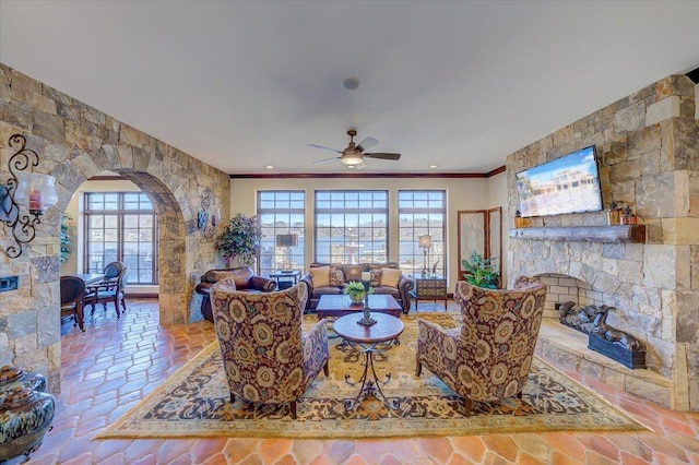 living room with crown molding, a stone fireplace, and ceiling fan