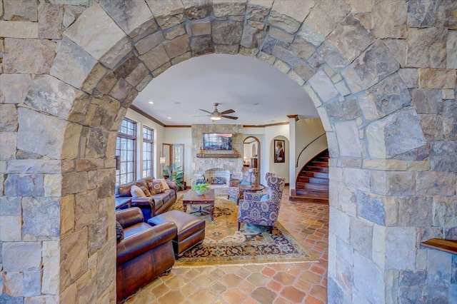 living room featuring crown molding, a stone fireplace, and ceiling fan