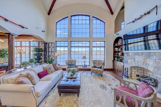 living room with built in features, lofted ceiling, a stone fireplace, and light hardwood / wood-style flooring