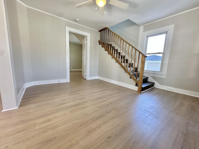 empty room with light wood finished floors, baseboards, a ceiling fan, stairs, and crown molding