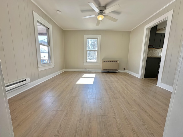 empty room with a baseboard heating unit, ornamental molding, light wood-style flooring, and baseboards