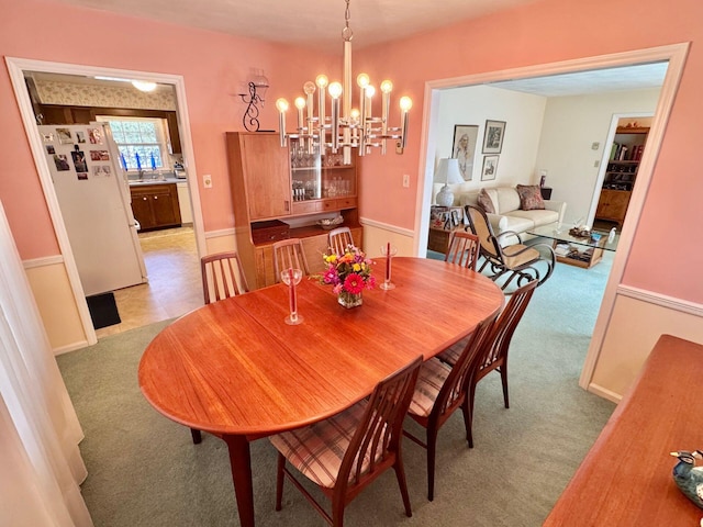 dining space with sink, light carpet, and a chandelier