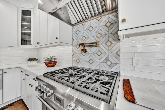kitchen featuring ventilation hood, white cabinets, stainless steel gas range, and glass insert cabinets