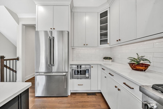 kitchen with freestanding refrigerator, wood finished floors, glass insert cabinets, white cabinetry, and tasteful backsplash