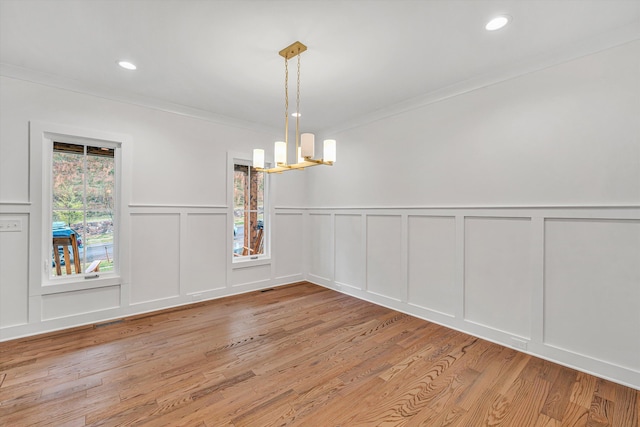 unfurnished dining area with an inviting chandelier, ornamental molding, a decorative wall, and light wood finished floors
