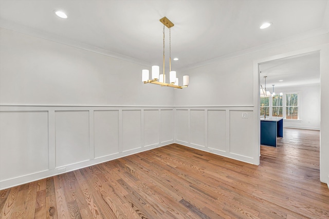unfurnished dining area featuring crown molding, a decorative wall, wood finished floors, recessed lighting, and a notable chandelier