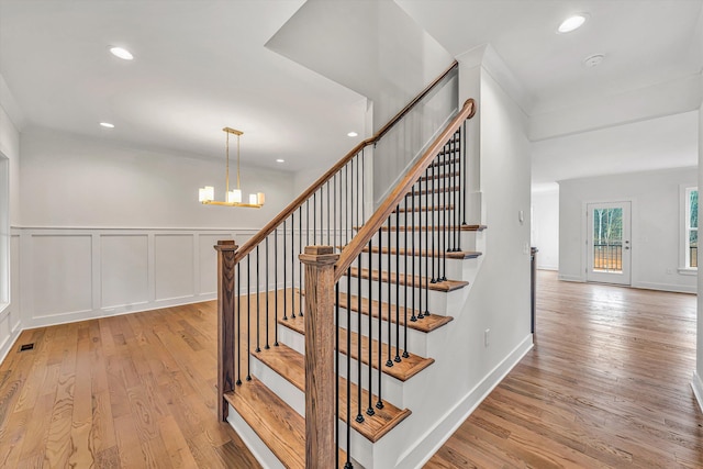 stairway with wood finished floors, a wainscoted wall, a chandelier, a decorative wall, and recessed lighting
