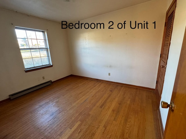 spare room featuring a baseboard heating unit and light wood-type flooring