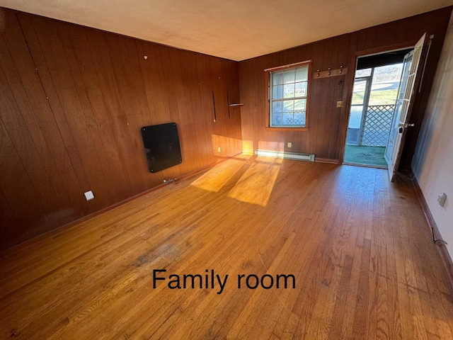 unfurnished living room with a baseboard radiator, hardwood / wood-style floors, and wooden walls