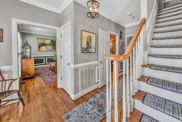 stairway featuring hardwood / wood-style floors, crown molding, and a notable chandelier