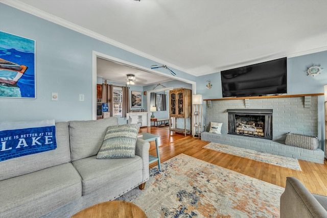 living room with crown molding, ceiling fan, a fireplace, and hardwood / wood-style floors