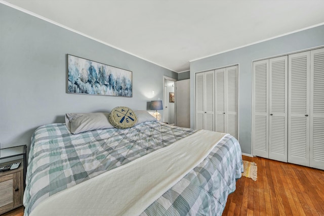 bedroom with hardwood / wood-style floors, crown molding, and multiple closets