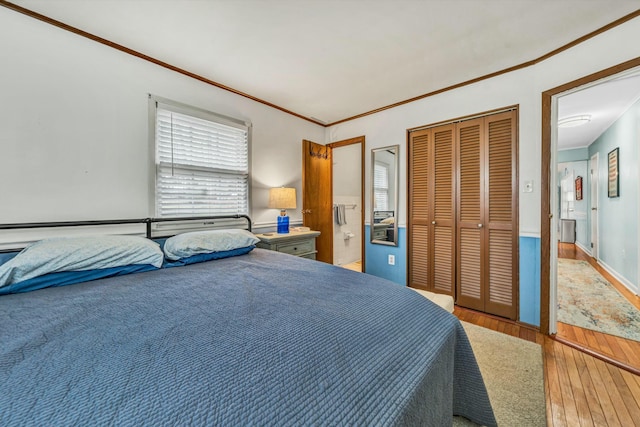 bedroom with wood-type flooring, connected bathroom, crown molding, and a closet