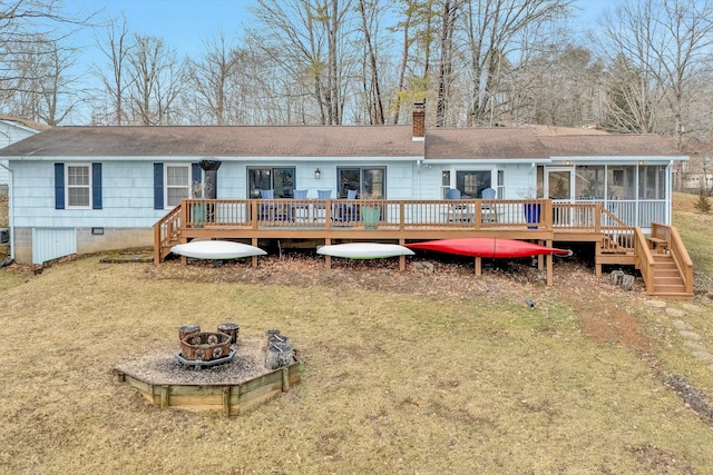 back of property featuring a yard, a deck, a sunroom, and an outdoor fire pit