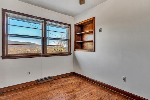 empty room with wood-type flooring, built in features, and ceiling fan