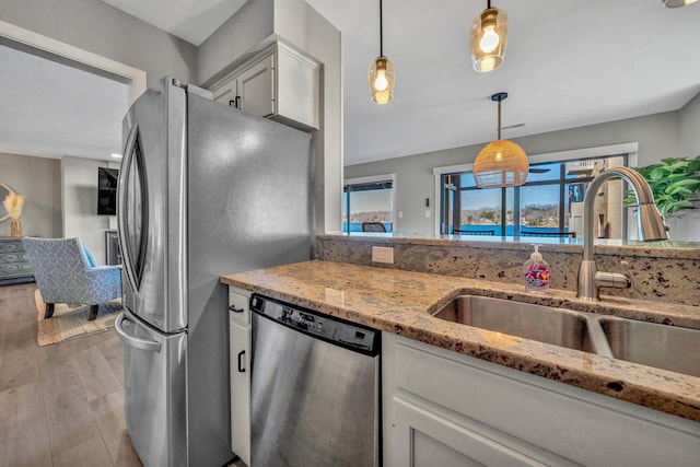 kitchen featuring appliances with stainless steel finishes, pendant lighting, sink, white cabinets, and light stone countertops