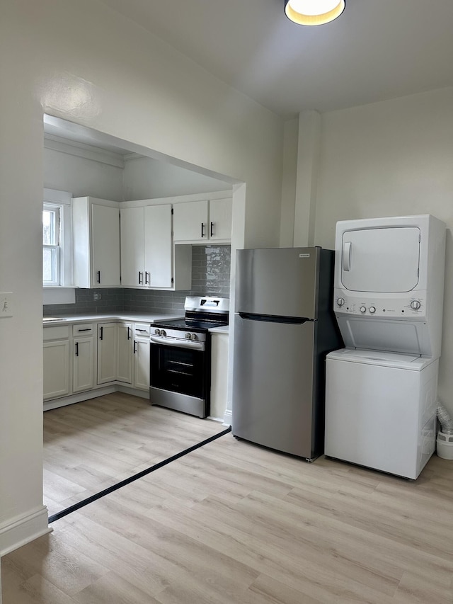 kitchen featuring decorative backsplash, white cabinets, appliances with stainless steel finishes, light wood-type flooring, and stacked washing maching and dryer