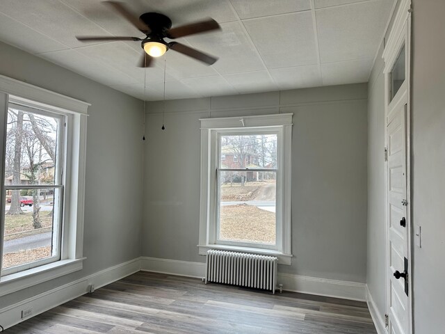 empty room with baseboards, wood finished floors, a wealth of natural light, and radiator