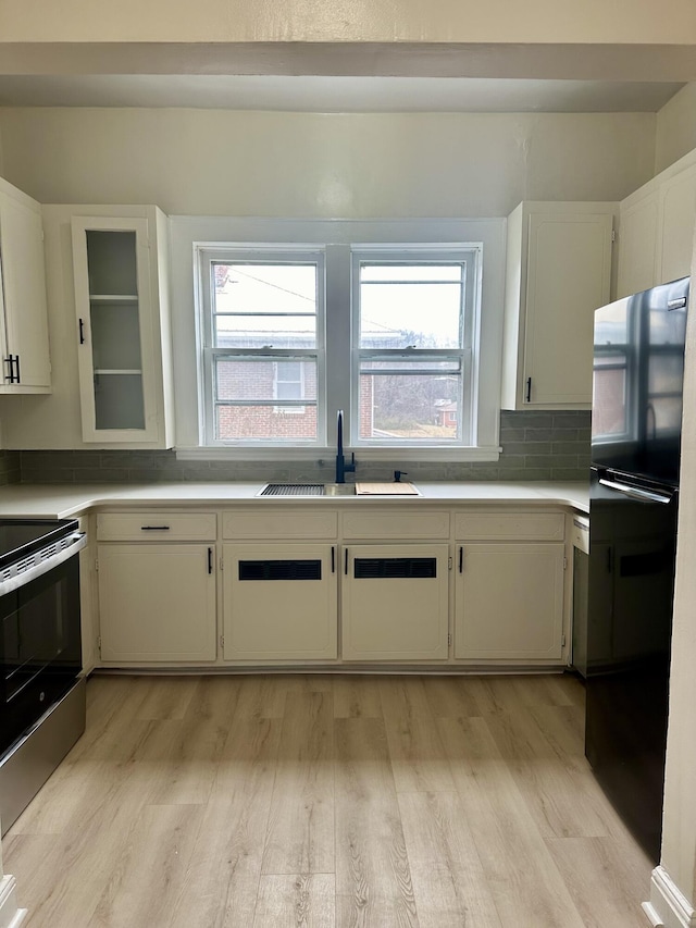 kitchen featuring a sink, light wood-style floors, stainless steel range with electric cooktop, a wealth of natural light, and freestanding refrigerator