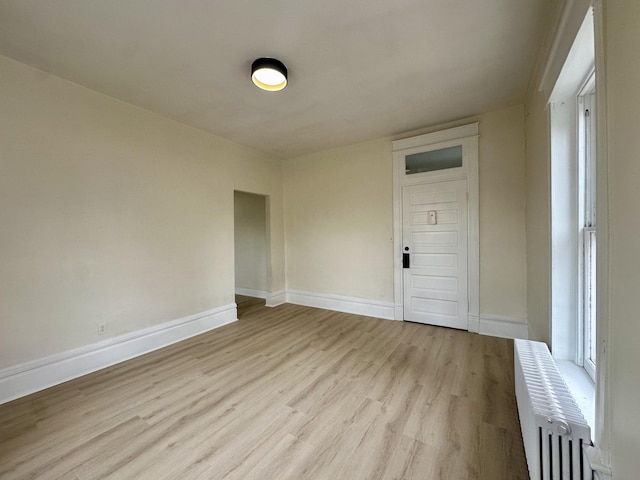 spare room with light wood finished floors, radiator heating unit, and baseboards