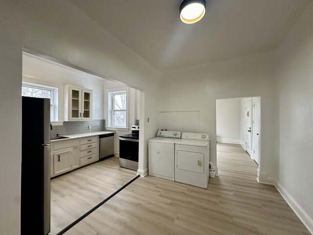 clothes washing area featuring baseboards, a sink, light wood-style flooring, and washer and dryer