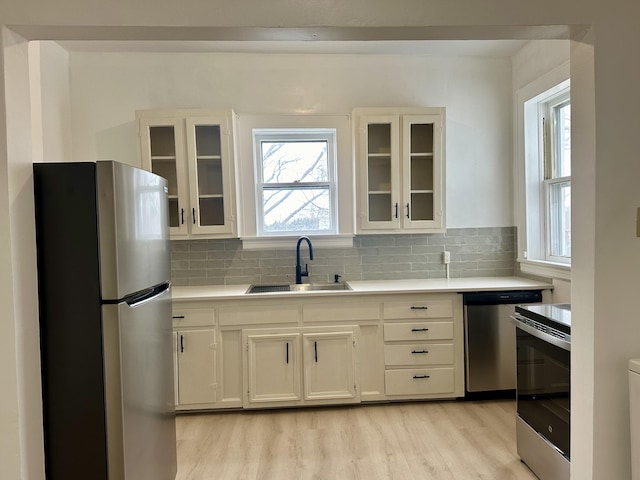 kitchen with a sink, stainless steel appliances, light countertops, light wood-type flooring, and backsplash