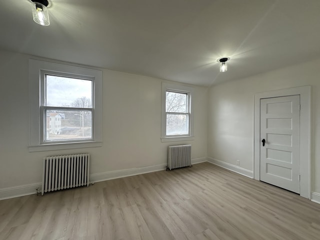 empty room featuring radiator heating unit, light wood-style flooring, and baseboards