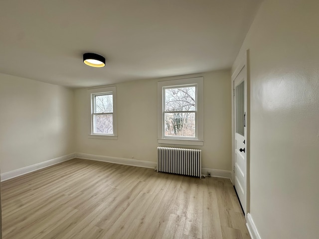 empty room with light wood-type flooring, radiator, and baseboards