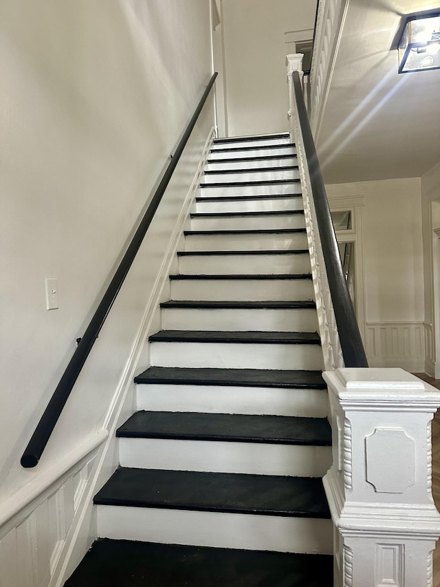 stairs featuring wainscoting and a decorative wall