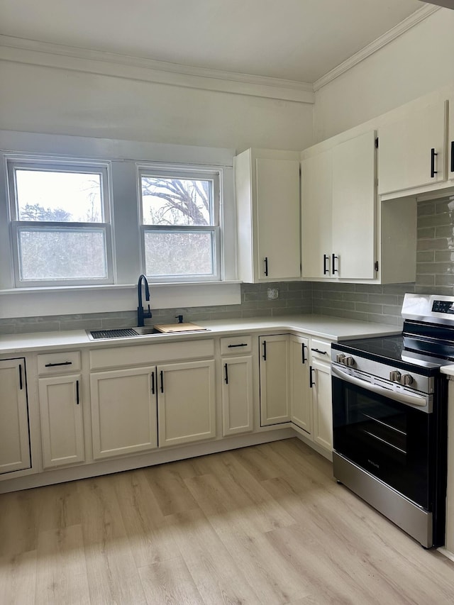 kitchen featuring electric range, decorative backsplash, light countertops, crown molding, and a sink