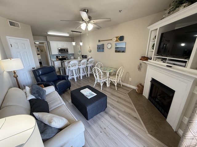 living room with ceiling fan, a fireplace, visible vents, baseboards, and light wood-type flooring