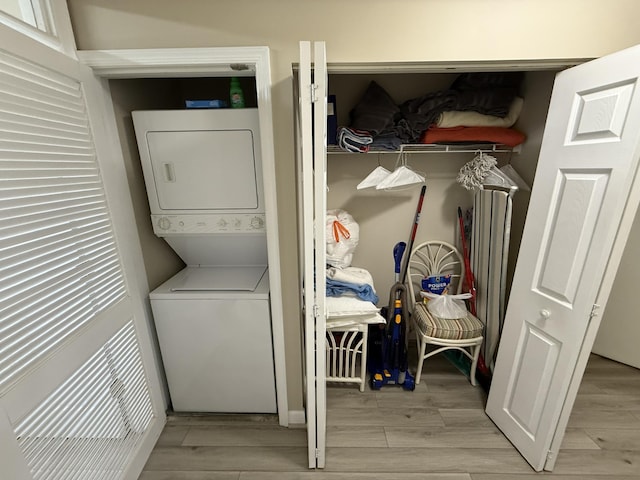 laundry room featuring wood finish floors, stacked washer and clothes dryer, and laundry area