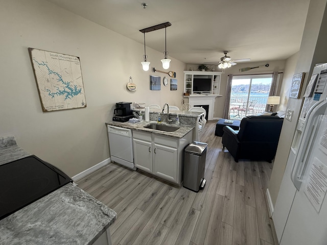 kitchen featuring a fireplace, white dishwasher, a sink, light wood-type flooring, and a peninsula