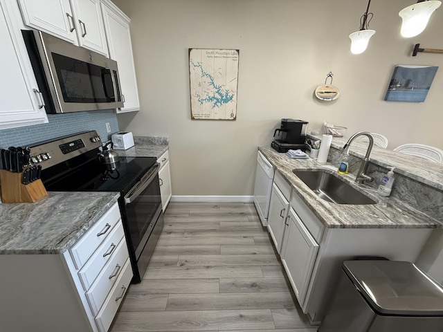 kitchen with backsplash, appliances with stainless steel finishes, light wood-style floors, a sink, and a peninsula