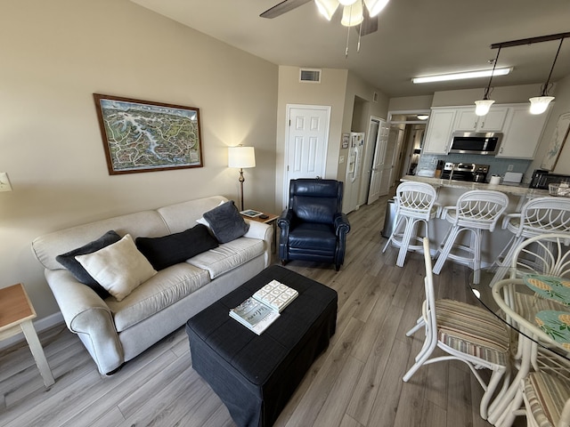 living area with light wood finished floors, visible vents, and a ceiling fan