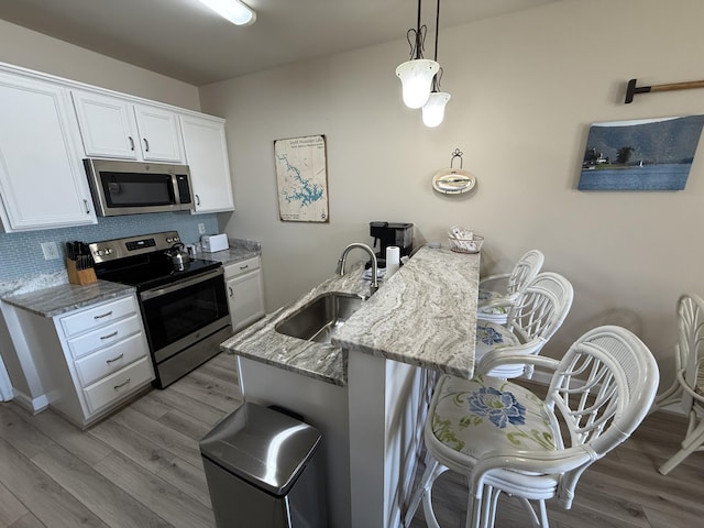 kitchen with white cabinets, appliances with stainless steel finishes, light stone countertops, light wood-style floors, and a sink