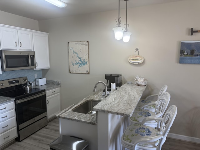 kitchen with appliances with stainless steel finishes, white cabinets, a sink, a peninsula, and a kitchen breakfast bar