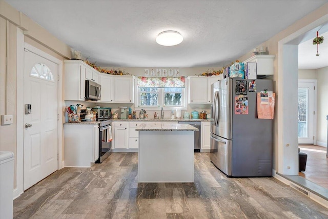 kitchen with sink, white cabinetry, light stone counters, a center island, and appliances with stainless steel finishes